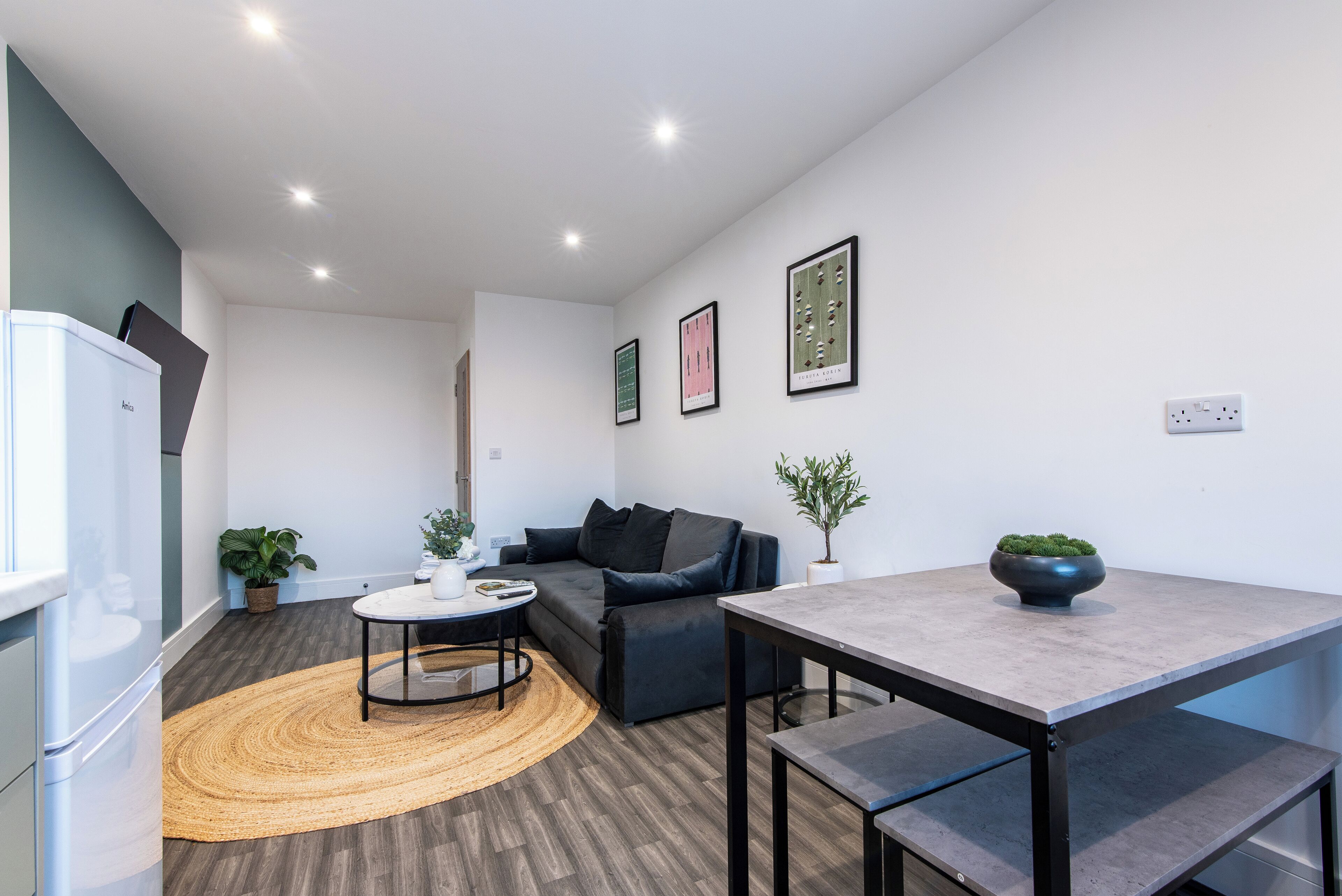 Una sala moderna con sofá, mesa de centro y mesa de comedor. Hay plantas en macetas y cuadros en las paredes.
