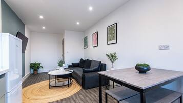 Una sala moderna con sofá, mesa de centro y mesa de comedor. Hay plantas en macetas y cuadros en las paredes.