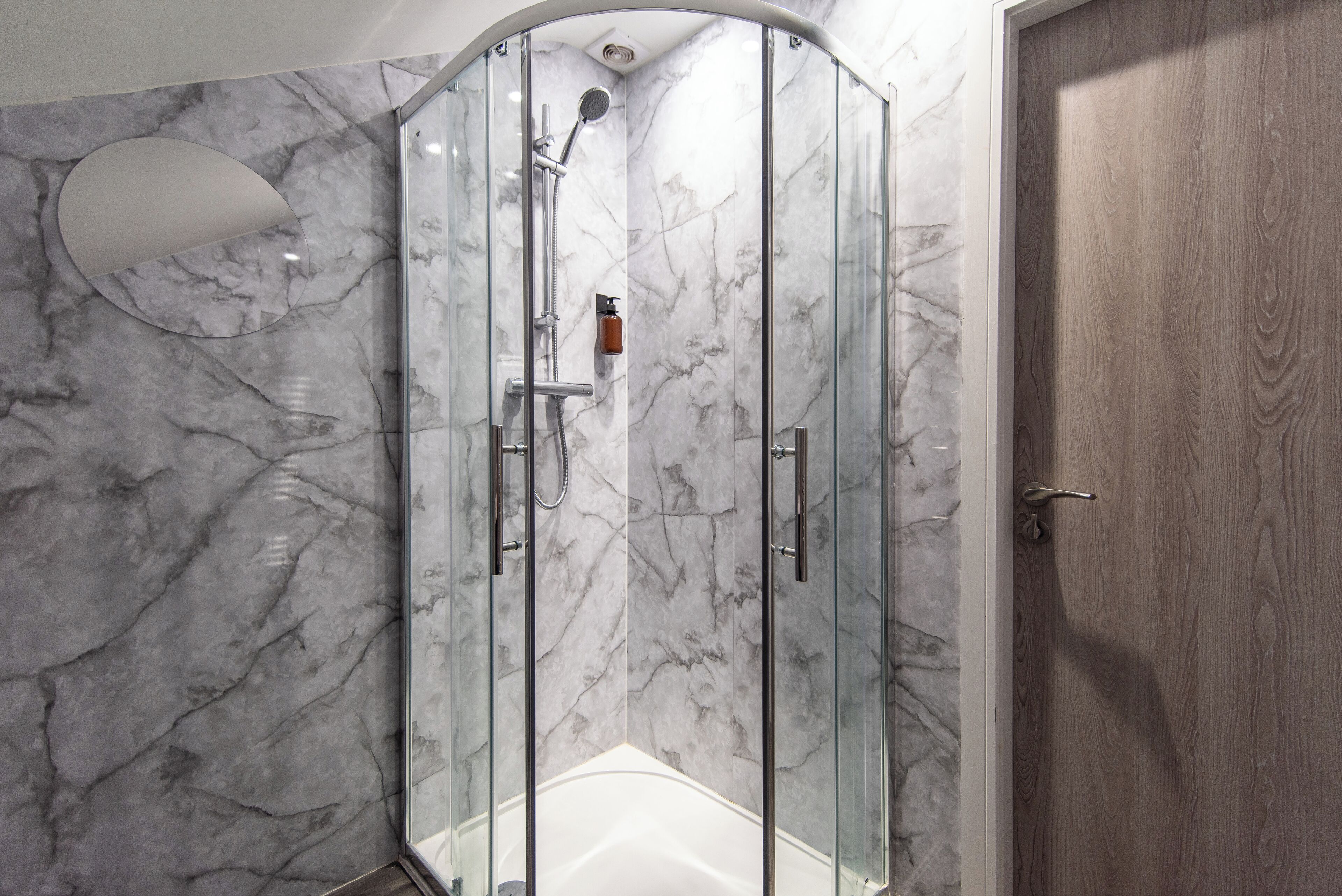 Eine Glaskabine mit Dusche, eine Marmorwand, eine Holztür und eine weiße Badewanne.