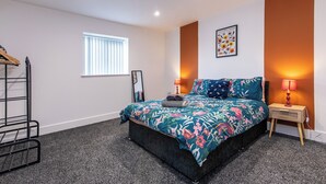 Une chambre à coucher comprenant un lit, une table de chevet, une lampe, une fenêtre et un tableau accroché au mur.