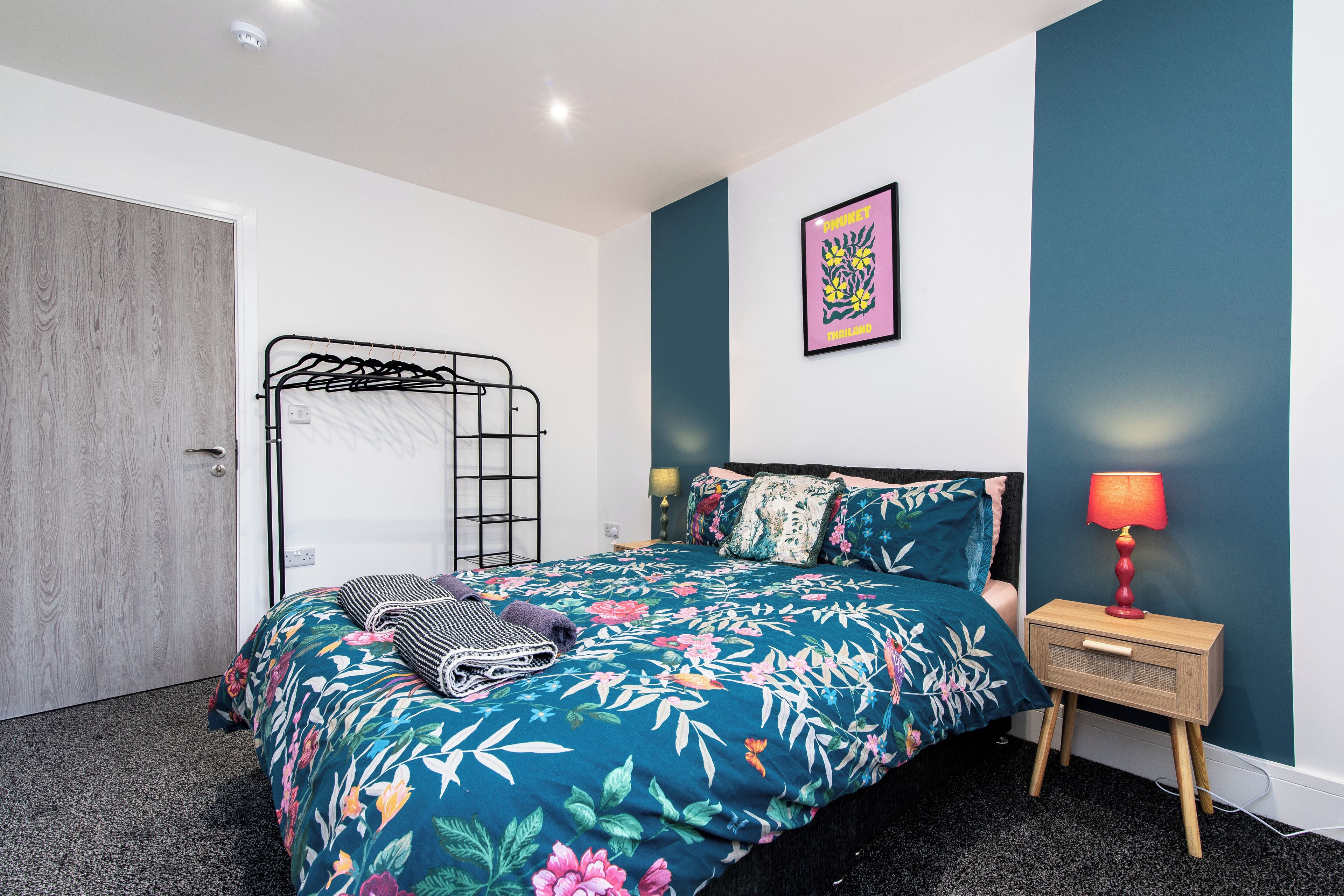 Un dormitorio con una cama, una mesita de noche con lámpara, un cuadro en la pared y una puerta.