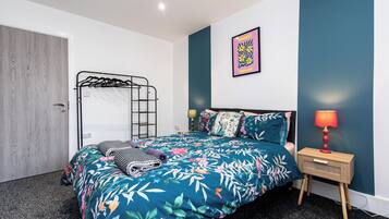Un dormitorio con una cama, una mesita de noche con lámpara, un cuadro en la pared y una puerta.