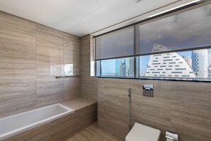 A modern bathroom with a bathtub, a toilet, and a shower. It features large windows with a view of tall buildings. - SIMPLY COMFORT Missoni Top Floor with Sea, Canal and Burj Khalifa Views (Dubai)