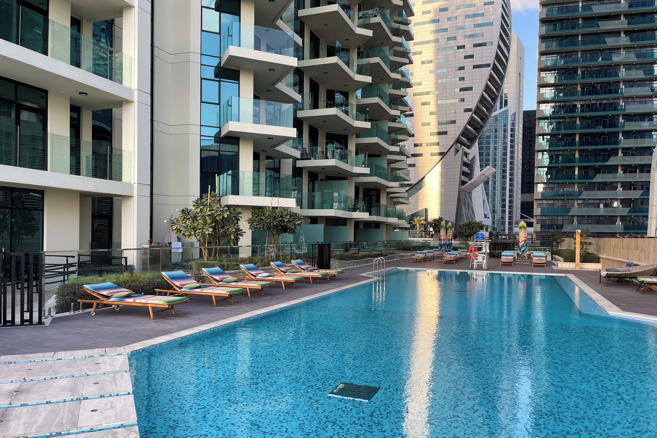 A modern hotel with a swimming pool, multiple balconies, and a view of surrounding buildings.