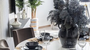 Une table à manger dressée avec des assiettes, des bols et des verres à vin noirs et blancs, entourée de chaises sombres.