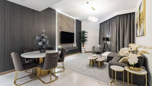 Un salon moderne avec une table à manger ronde, des canapés gris et un téléviseur à écran plat fixé au mur.