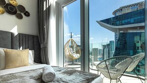 Une chambre d’hôtel moderne avec un grand lit, une vue sur la ville et un balcon équipé de chaises.
