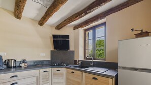 A kitchen with wooden cabinets, a built-in oven, a sink, and a window with a view of greenery. - Lovely house with jacuzzi for 8 people (Mauzens-et-Miremont)