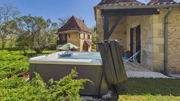 A hot tub in a garden with a stone building and a smaller structure in the background. - Lovely house with jacuzzi for 8 people (Mauzens-et-Miremont)
