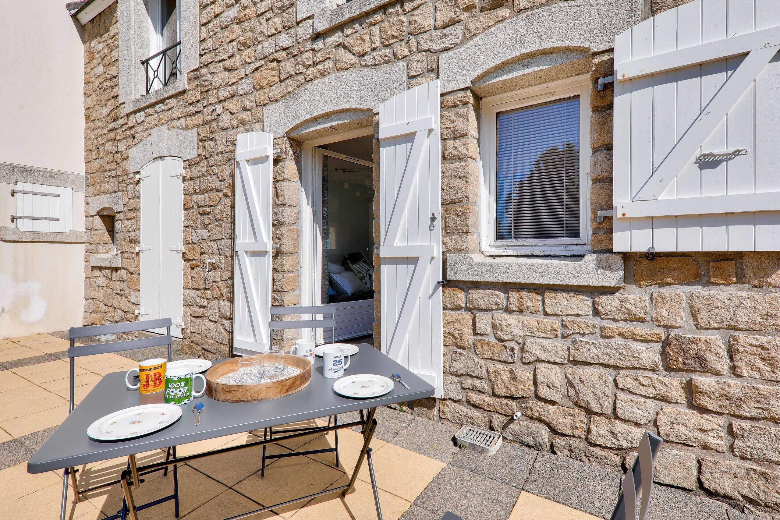 A stone building with a table set for two, a window with shutters, and a door.