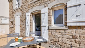 Un edificio de piedra con una mesa dispuesta para dos, una ventana con contraventanas y una puerta.