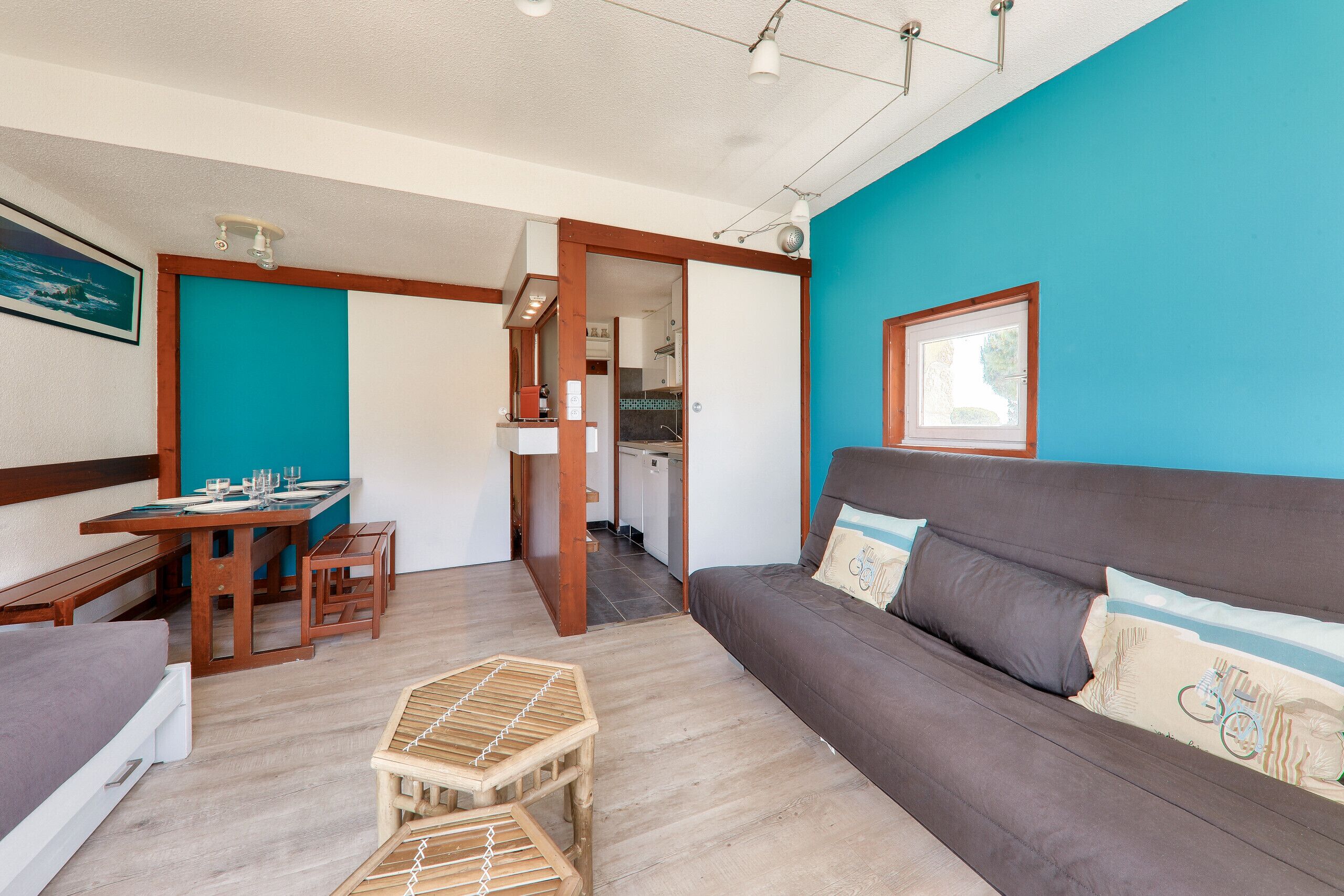 Ein Zimmer mit einer Holzbank, einem kleinen Holztisch, einer Couch mit Kissen und einem Esstisch für zwei Personen.