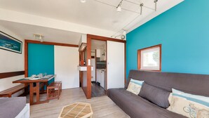 Una habitación con un banco de madera, una pequeña mesa de madera, un sofá con cojines y una mesa de comedor lista para dos.