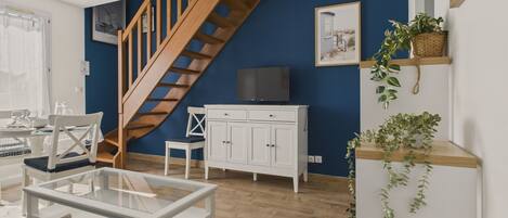 A modern living room with a wooden staircase, white furniture, and a television on a cabinet.