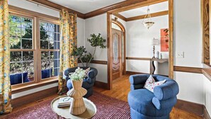 A room with a large window, a blue armchair, a wicker side table, and a wooden door. - Gold Leaf Chalet (Helen)