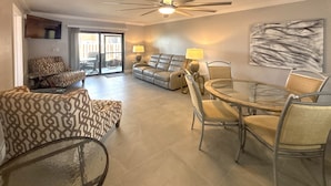 A spacious living area with a sofa, armchair, and dining table with chairs. - Vacation At Bac Bay! Fun In The Sun! 2B/2B Condo Walk To Beach! (Fort Myers Beach)