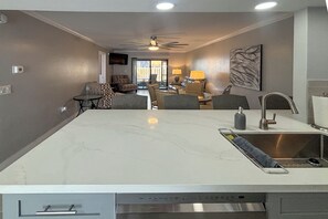 A modern kitchen with a central island, a built-in dishwasher, and a ceiling fan. - Vacation At Bac Bay! Fun In The Sun! 2B/2B Condo Walk To Beach! (Fort Myers Beach)