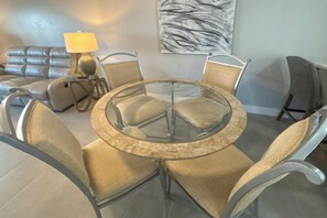 A dining area with a glass table surrounded by cushioned chairs, a sofa, and a lamp.