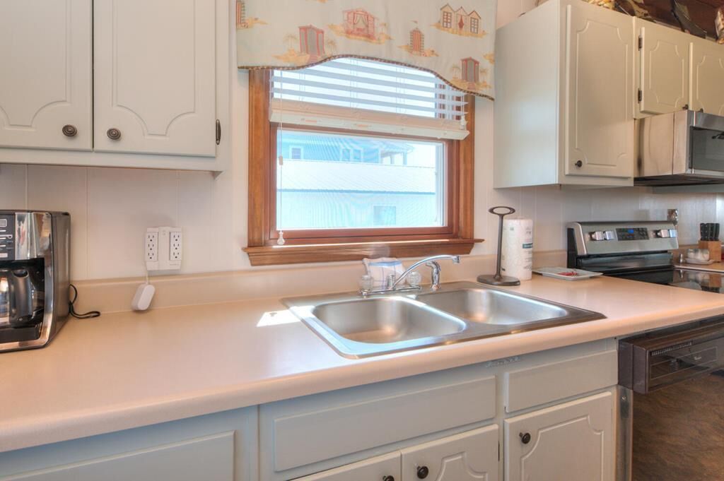 A kitchen with white cabinets, a double sink, a window with blinds, a toaster, and a dishwasher.