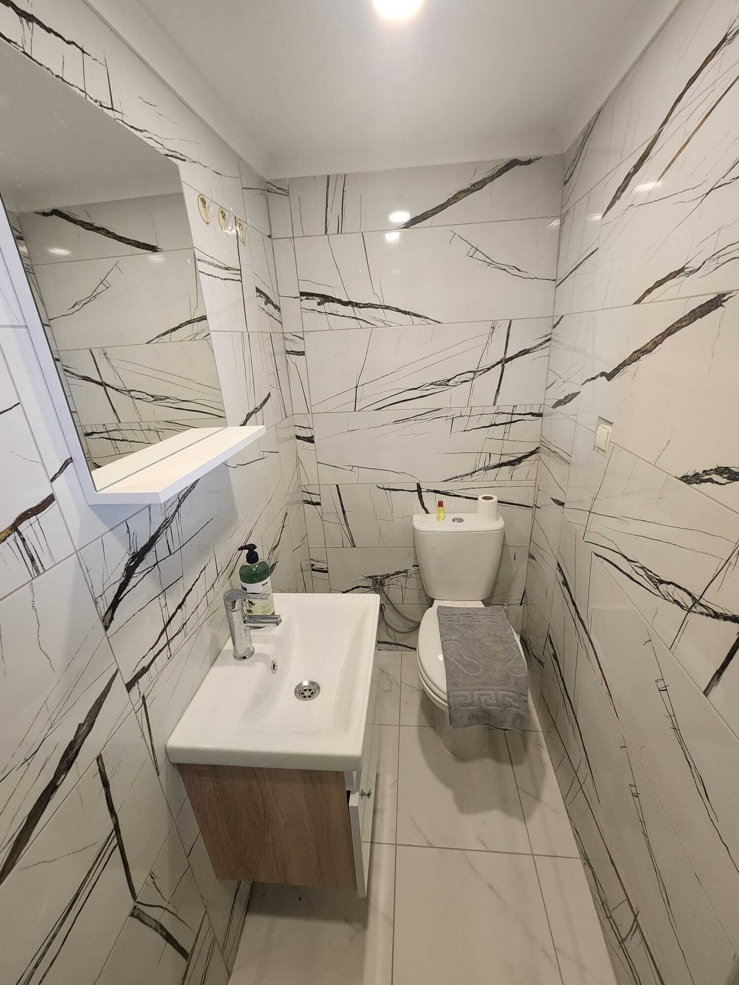 A bathroom with white marble tiles, a white sink, a toilet, and a mirror above the sink.