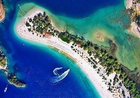 An aerial view of a coastal resort with a long sandy beach, a marina, and lush greenery.
