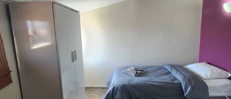 A small, compact room with a bed, a wardrobe, and a desk.