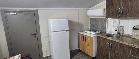 A compact kitchen with a refrigerator, stove, and wooden cabinets.
