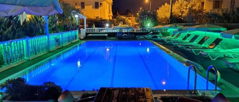 A swimming pool with a white fence, lounge chairs, and a covered area with umbrellas.