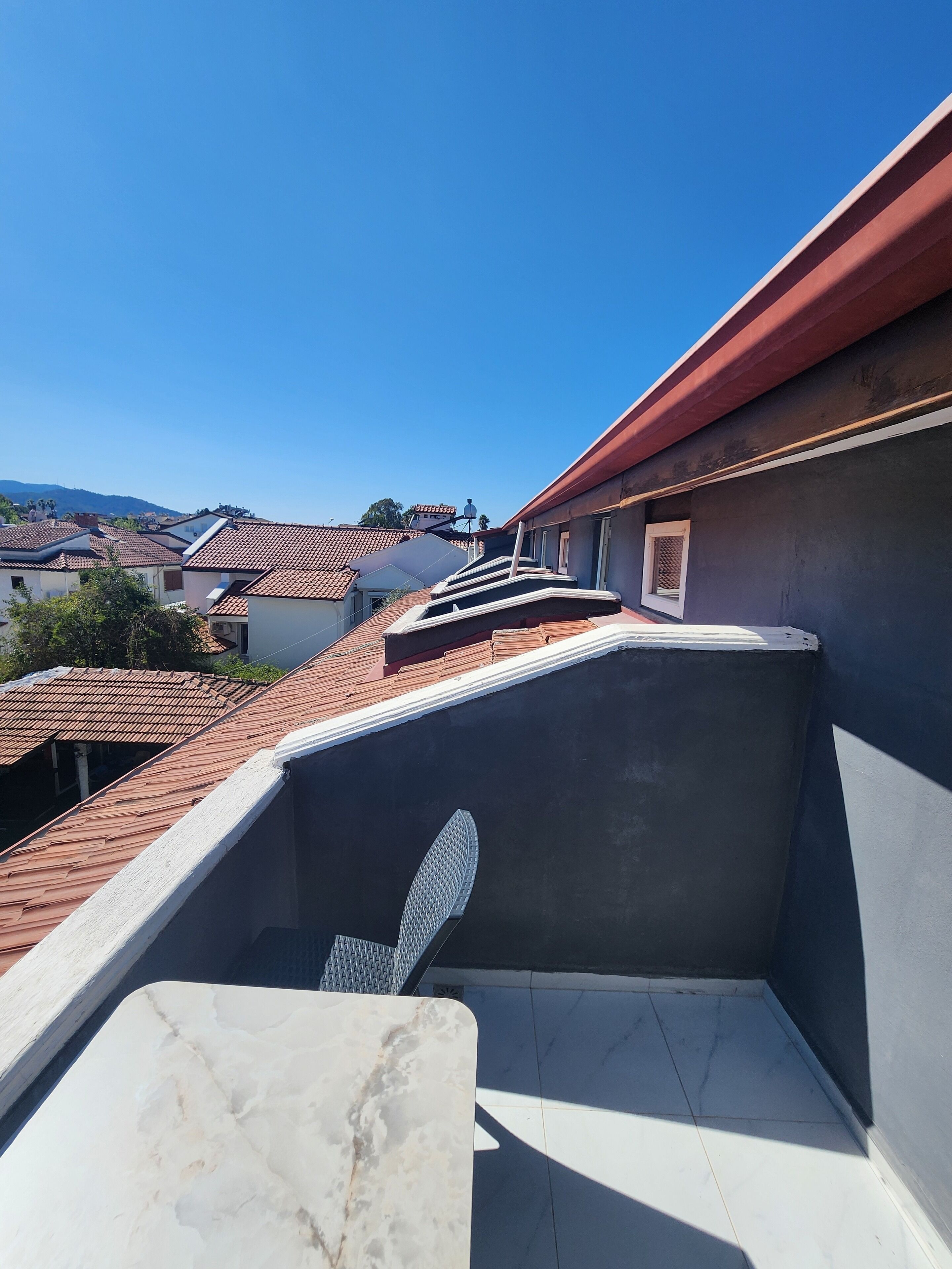 A rooftop terrace with a view of neighboring houses and a clear sky.