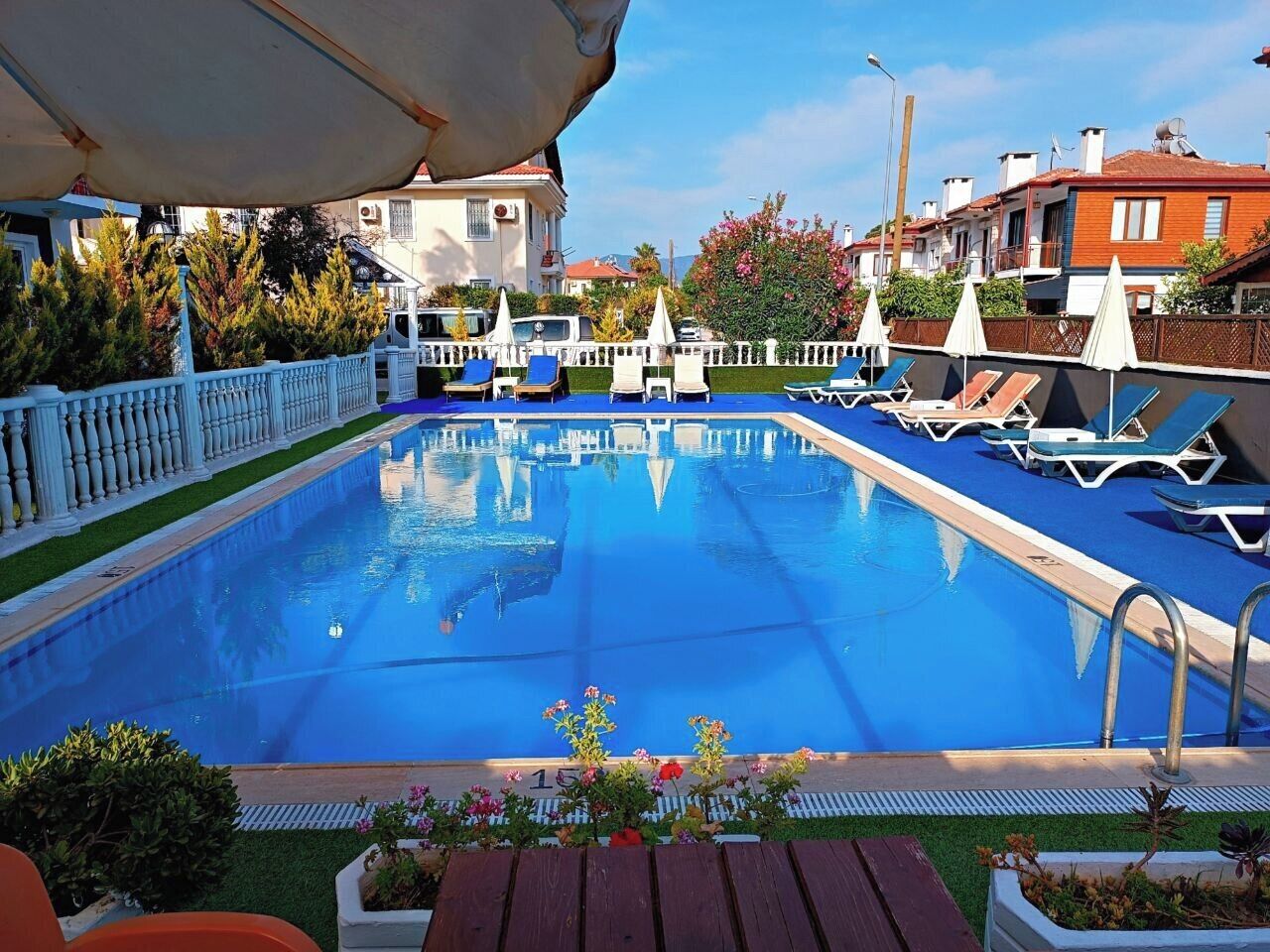 A rectangular swimming pool with clear blue water, surrounded by white railings and lounge chairs.