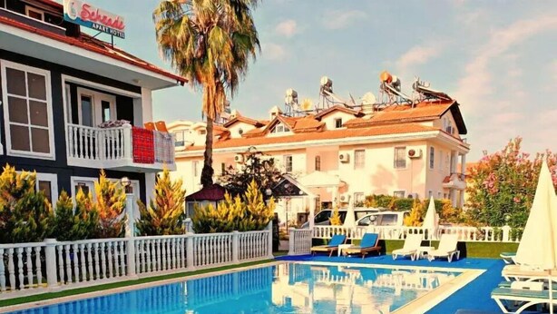 Ein Pool mit Liegestühlen, ein weißer Zaun und ein Gebäude mit Balkon im Hintergrund.
