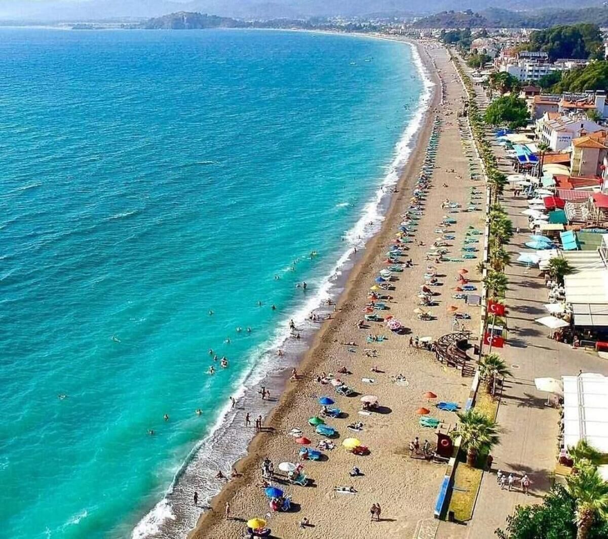 A beach with a row of beachside buildings, a clear blue sea, and people enjoying the beach.