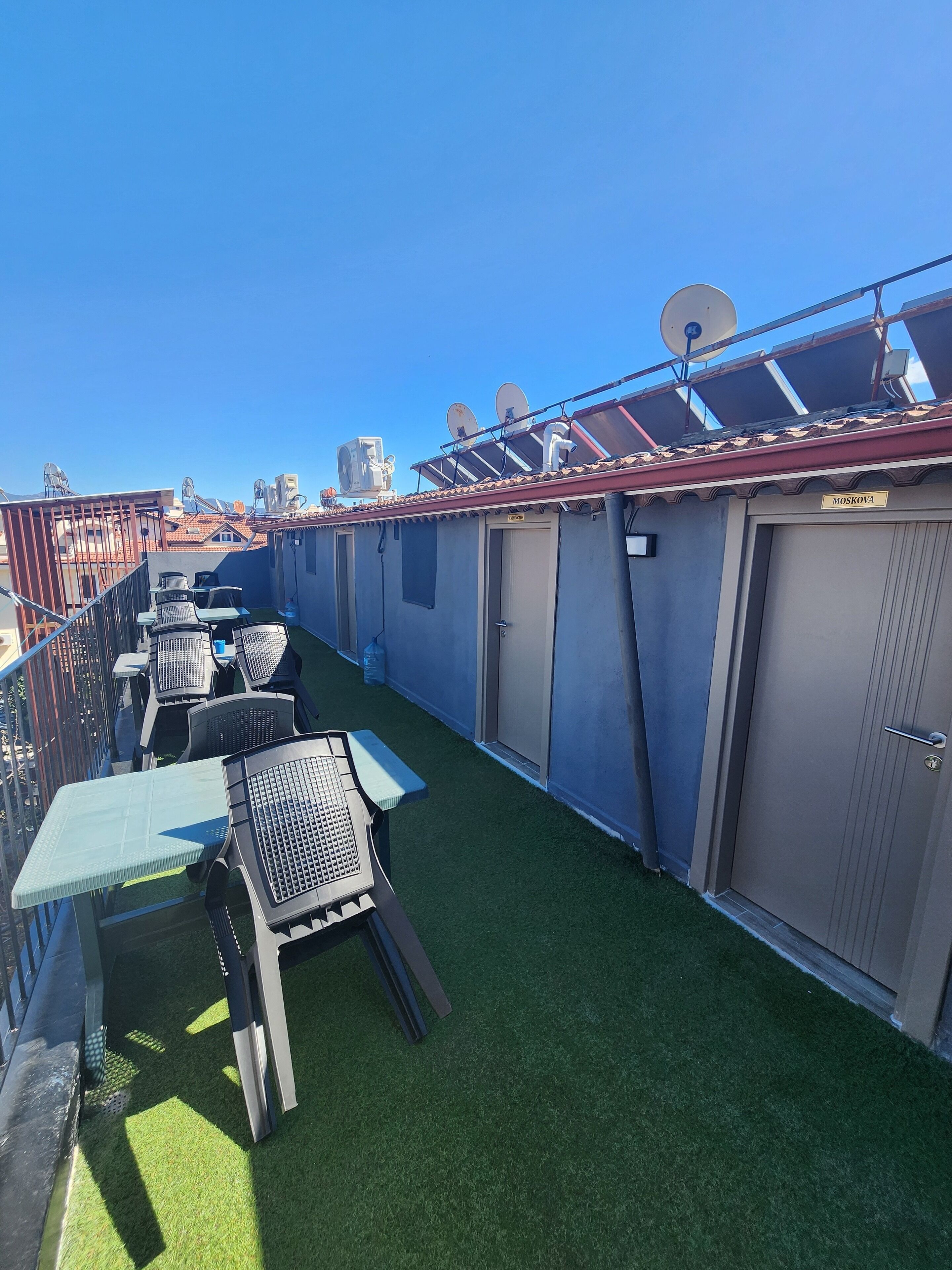Een dakterras met kunstgras, tuinmeubels en een rij grijze bergingen.