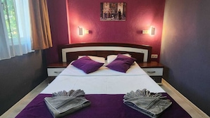 Ein Hotelzimmer mit einem großen Bett, violetter Bettwäsche, zwei Nachttischlampen und einem gerahmten Bild an der Wand.