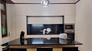 Μια μοντέρνα κουζίνα με μαύρο πάγκο, λευκά ντουλάπια, εντοιχισμένο φούρνο, μηχανή καφέ και ένα φωτιστικό οροφής.