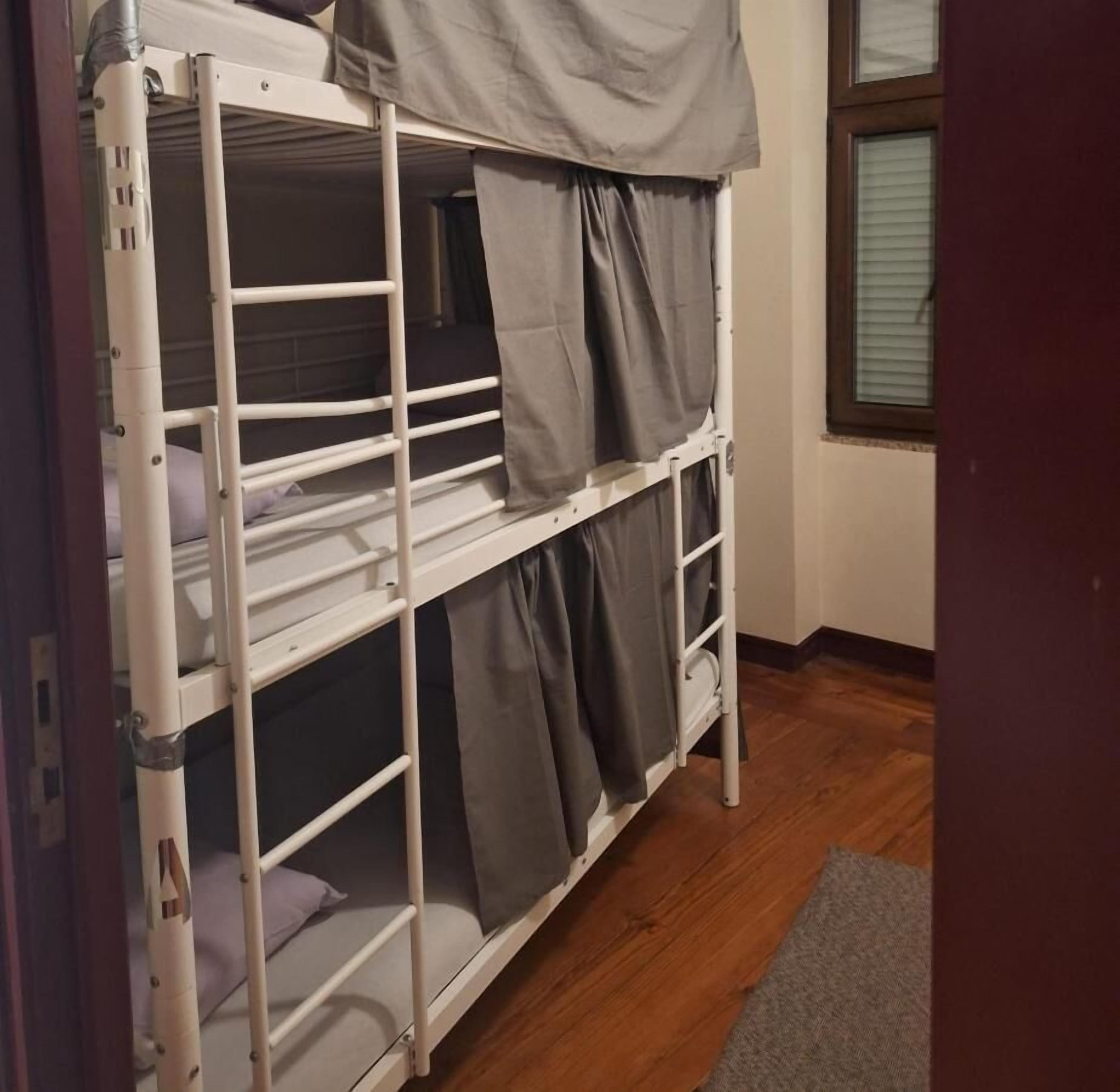 A bunk bed with grey curtains, a wooden floor, and a window with blinds.