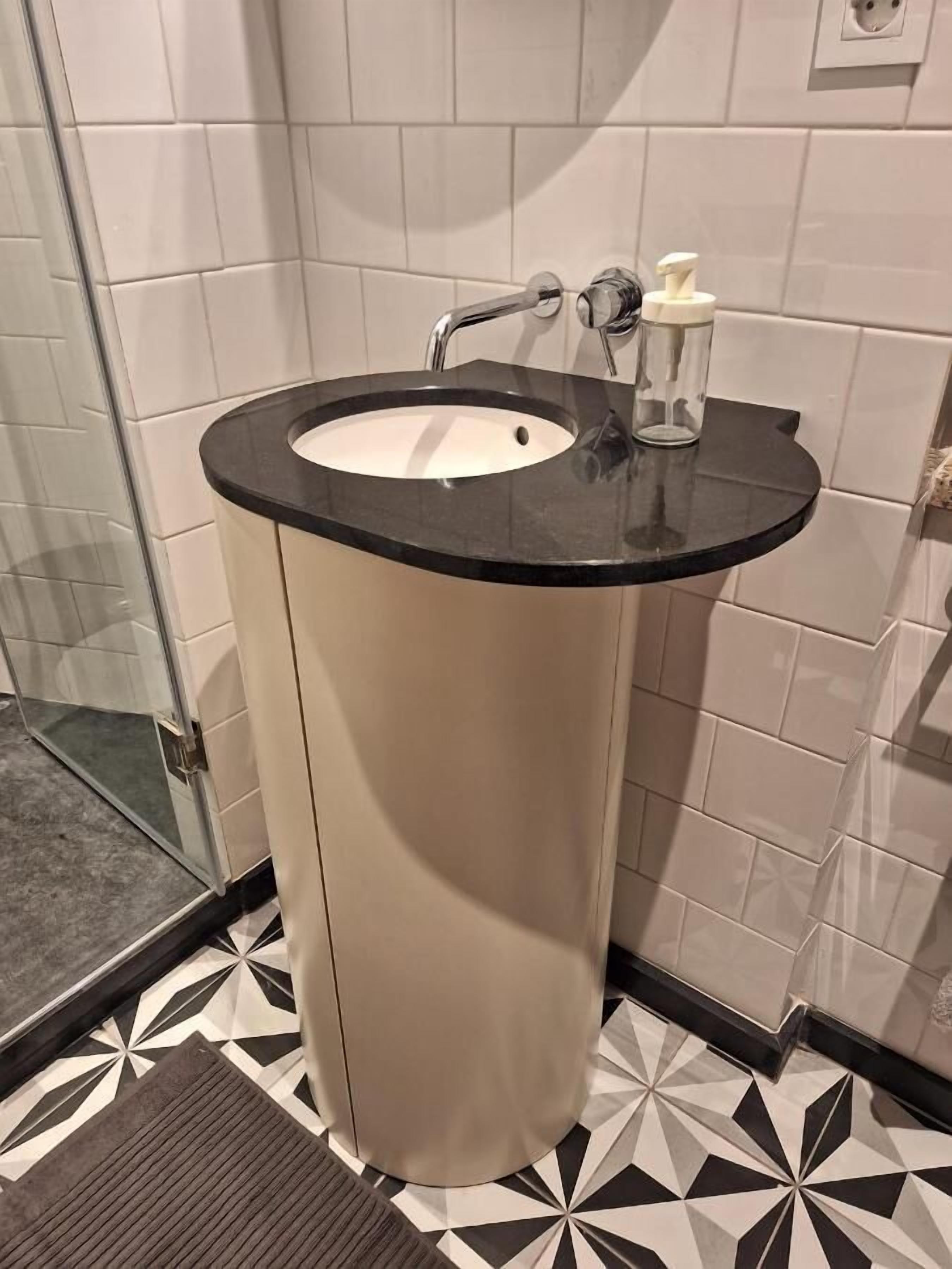 A bathroom with a round sink, a mirror, and a soap dispenser.