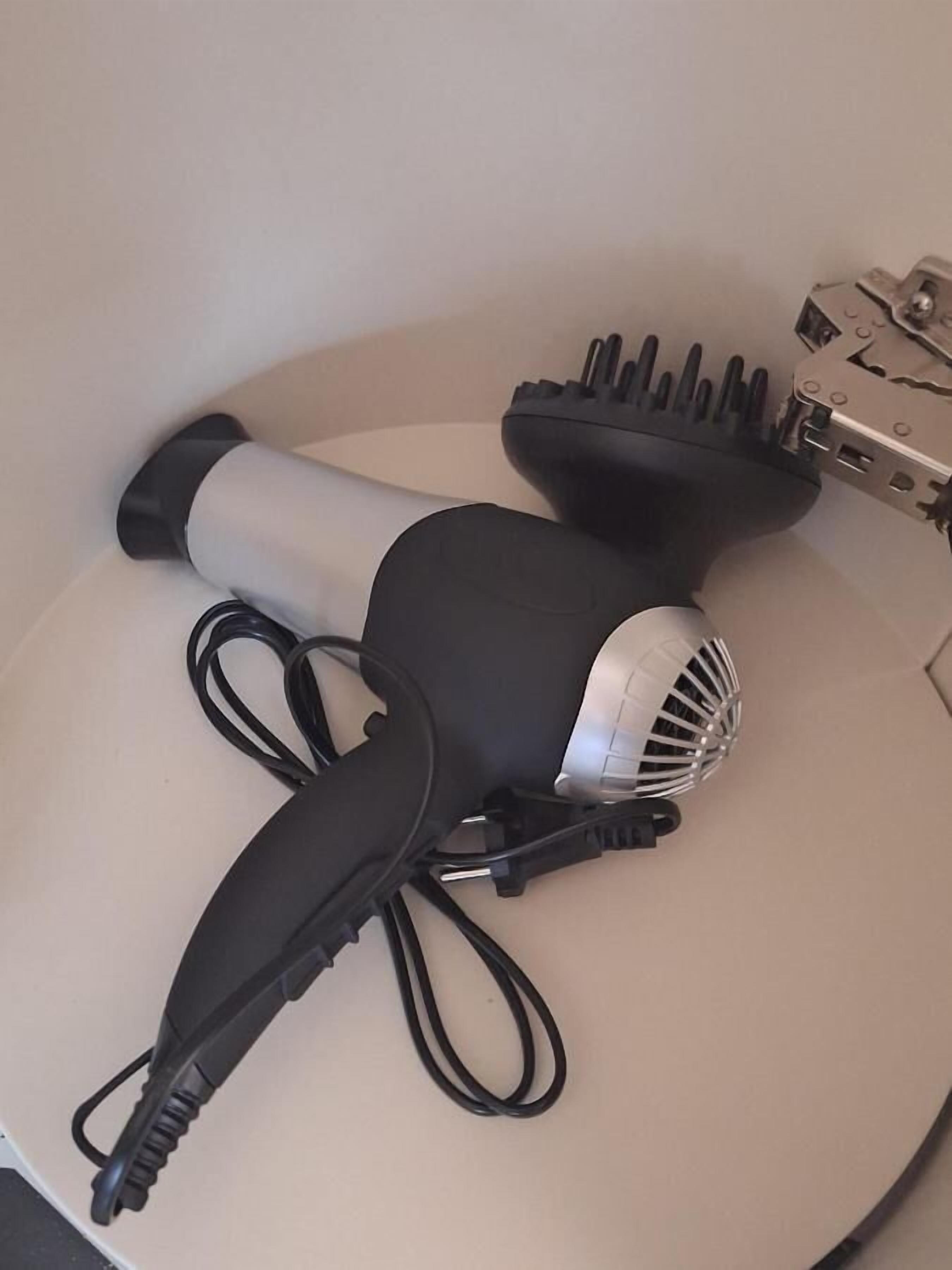 Ein Haartrockner mit Kabel und einer Mehrfachsteckdose auf einer weißen Oberfläche.