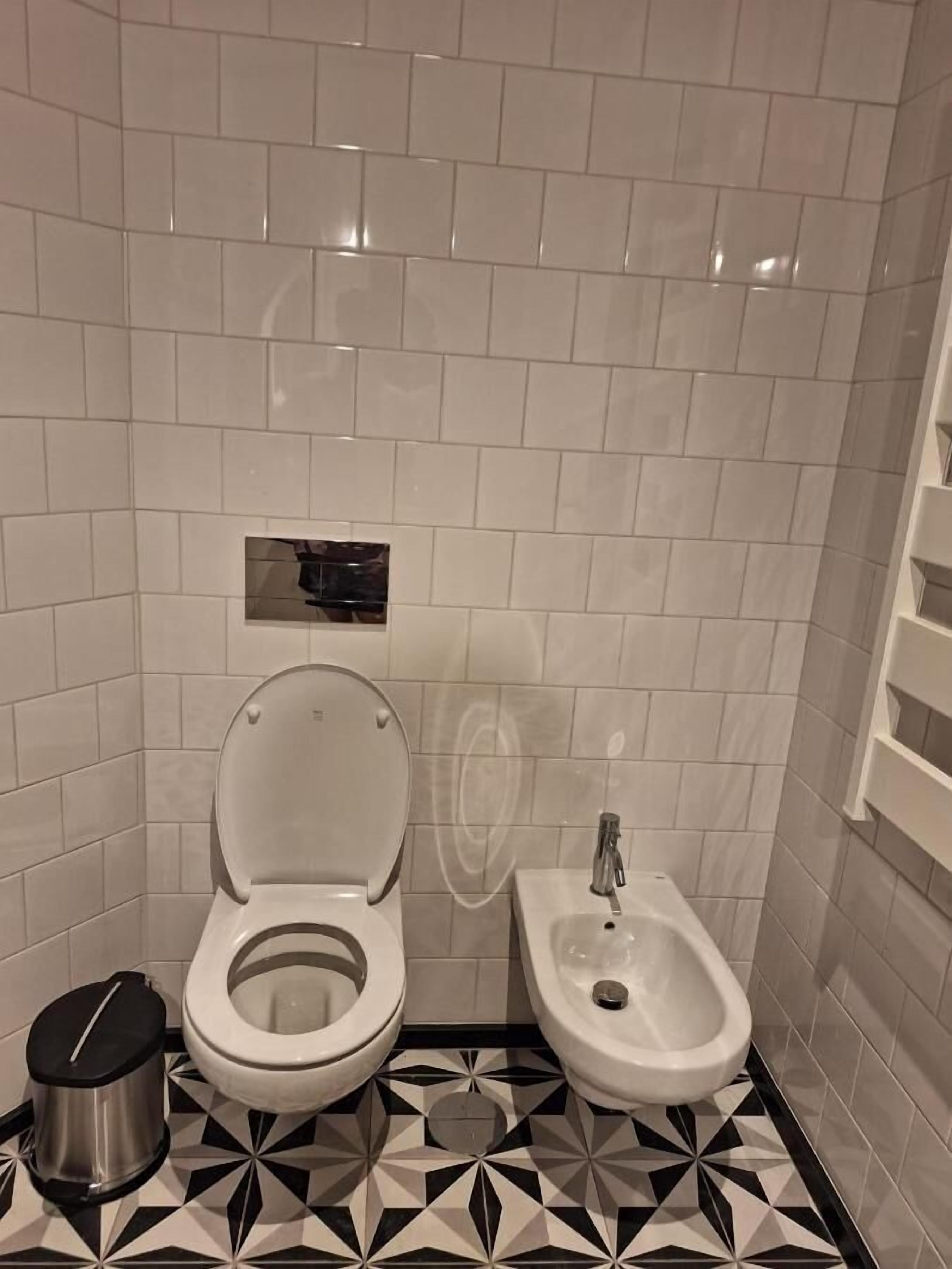 Un baño con inodoro, bidé y cubo de basura.