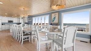 A spacious dining area with white chairs and a large table, overlooking a beach. - Grand View, Ocean Isle Beach (Ocean Isle Beach)