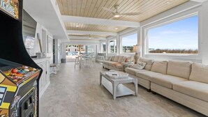 A spacious living area with a large window, a ceiling fan, and a retro arcade machine. - Grand View, Ocean Isle Beach (Ocean Isle Beach)