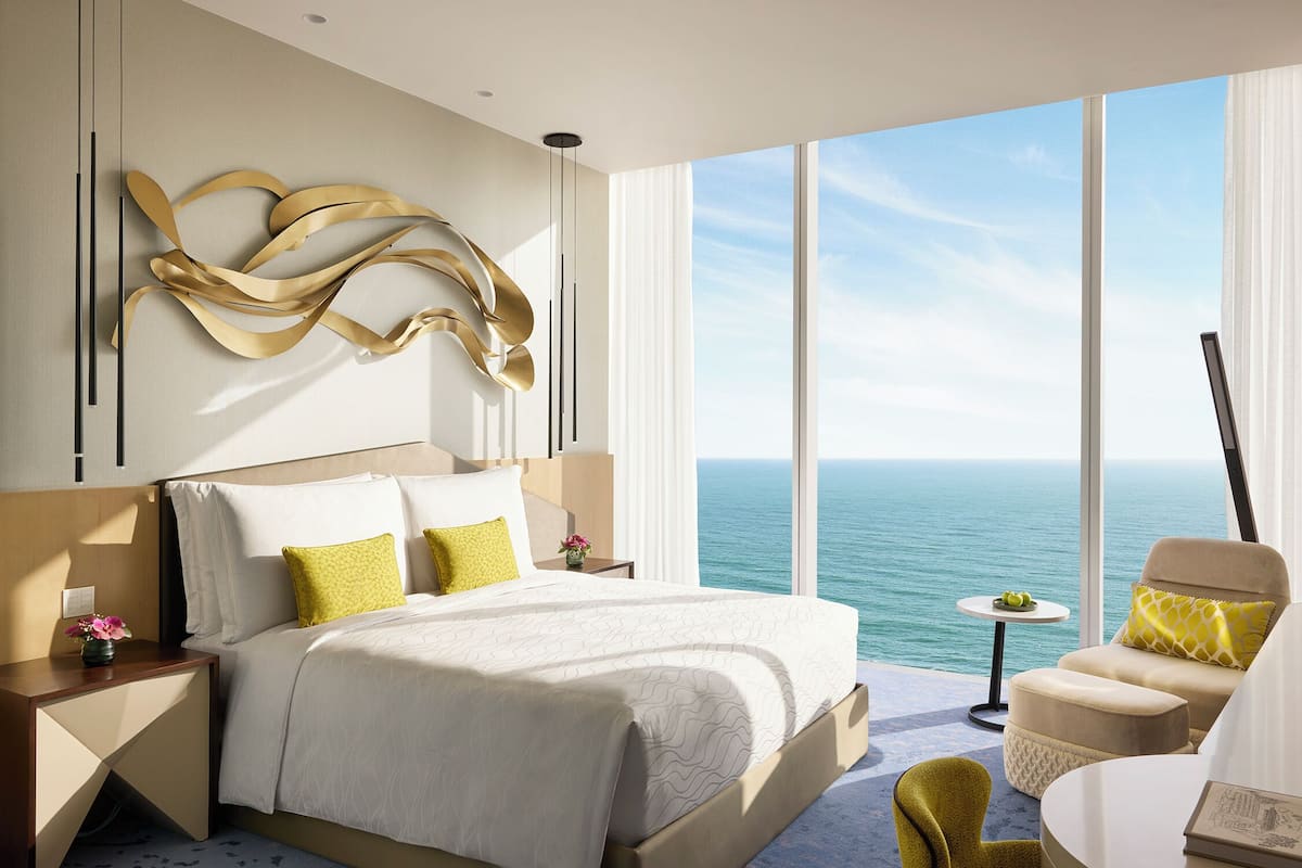 A modern hotel room with a large bed, a seating area, and a view of the ocean.