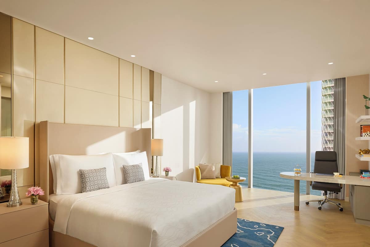 A modern hotel room with a large bed, a desk, and a view of the ocean.