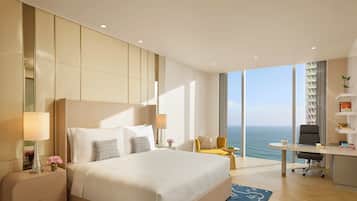 A modern hotel room with a large bed, a desk, and a view of the ocean.