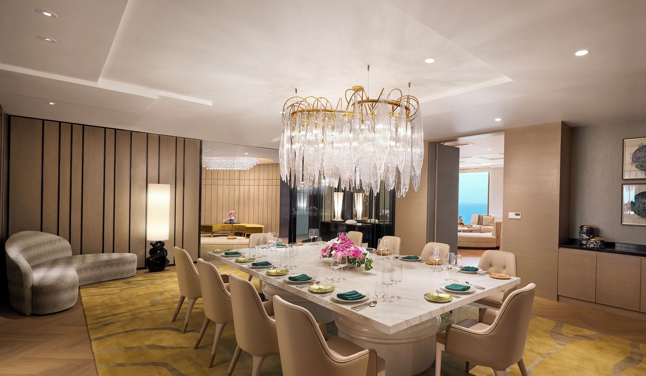 A modern dining room with a marble table, beige chairs, and a chandelier.