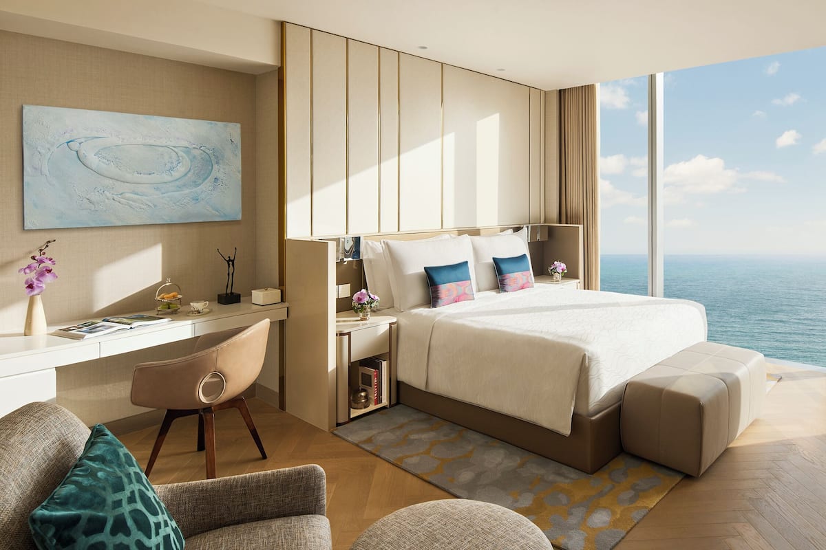 A modern bedroom with a large bed, a desk, and a view of the ocean.
