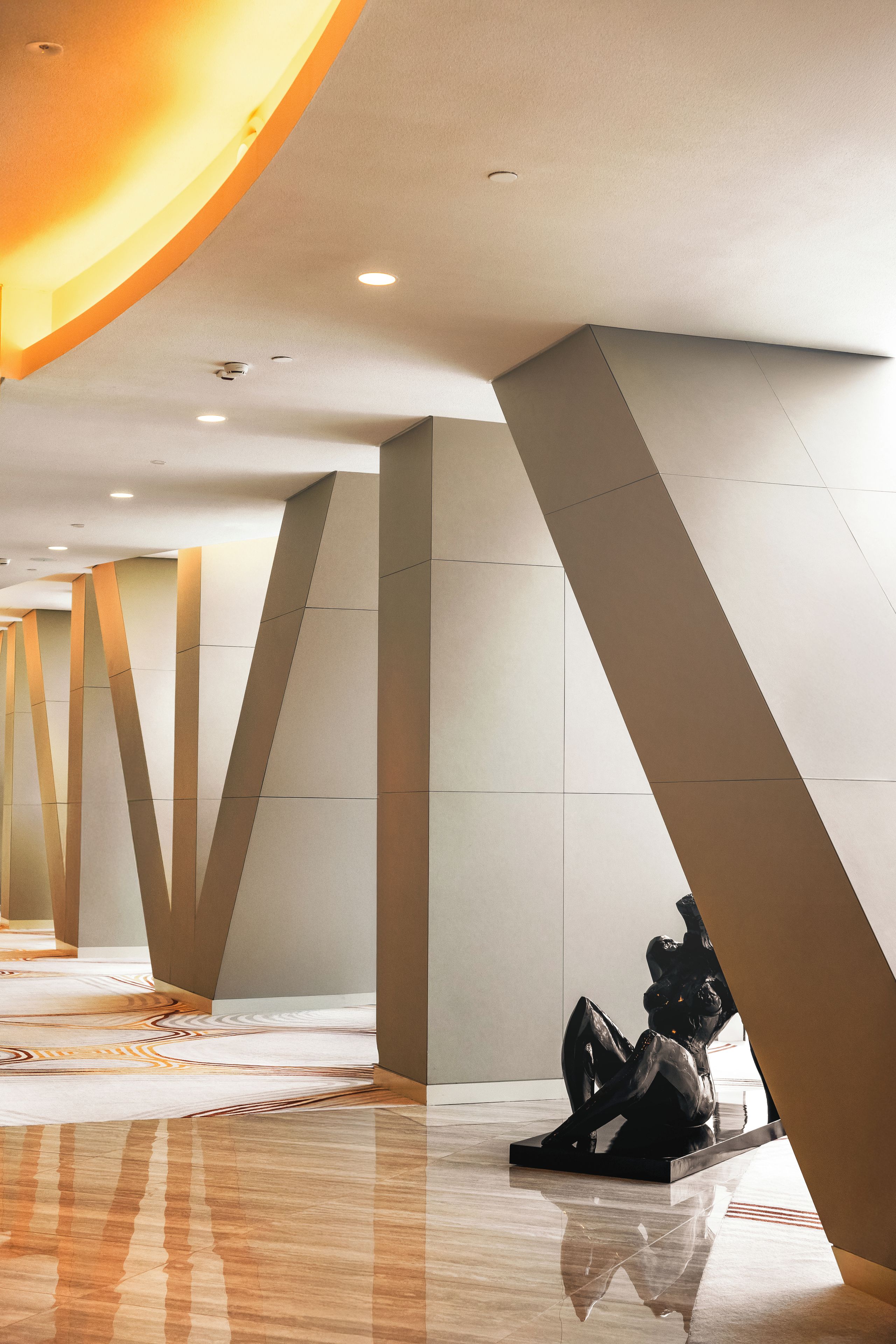 A modern interior with geometric ceiling design, reflective flooring, and a sculpture.