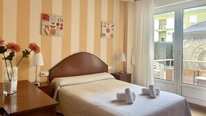 Ein Hotelzimmer mit Bett, Schreibtisch, Stuhl, Fenster mit Blick und einem Balkon.