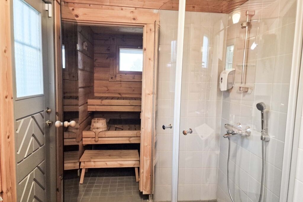 A wooden sauna with benches and a shower area with a tiled wall and showerhead.