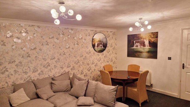 A cozy living room with a sectional sofa, a round dining table, and two chairs. A chandelier hangs from the ceiling, and there is a framed picture on the wall. - 3 Bed House - Sleeps 6 - Parking - Wifi (Maidstone)